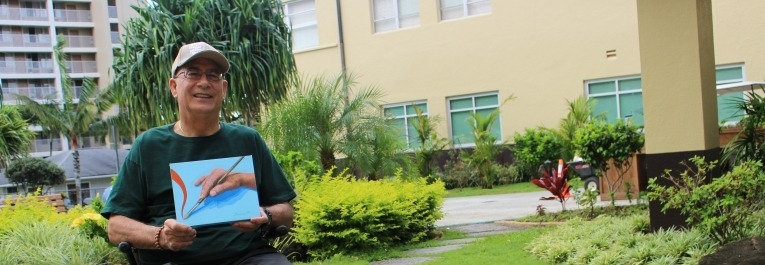 Spinal cord injury survivor, Dennis Okada, holding one of his paintings